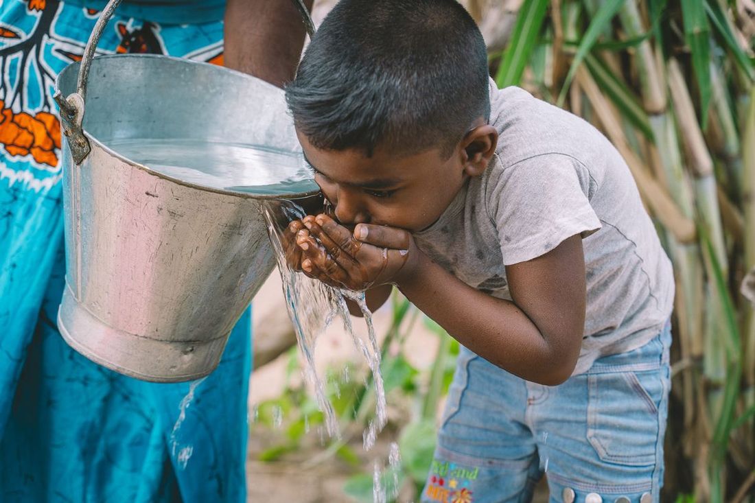A boy drinks water carried in a bucket